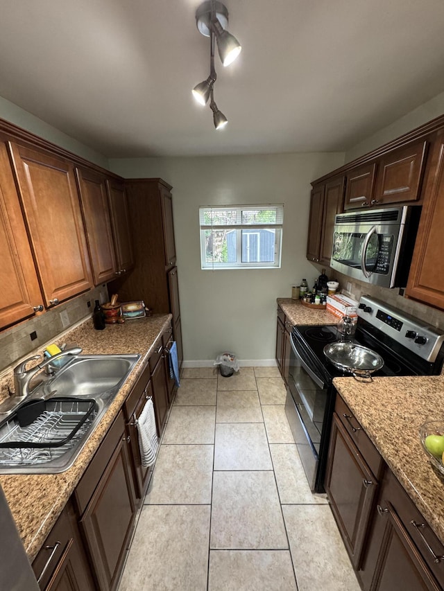 kitchen featuring stainless steel microwave, a sink, backsplash, light tile patterned floors, and electric range