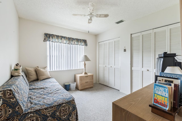 carpeted bedroom featuring multiple closets, visible vents, ceiling fan, and a textured ceiling