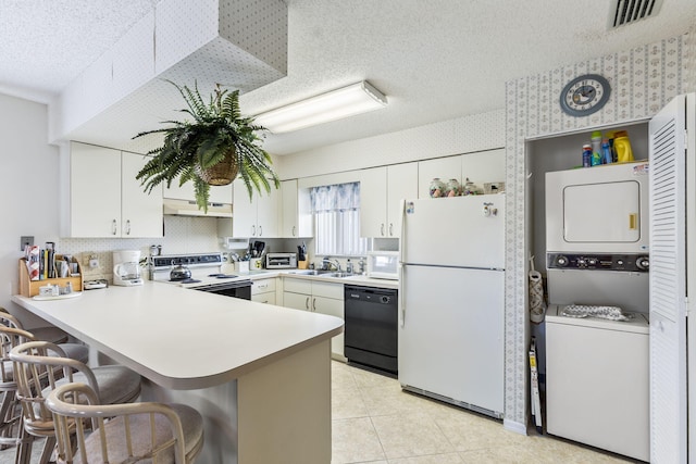 kitchen with stacked washer and dryer, visible vents, a textured ceiling, white appliances, and a peninsula