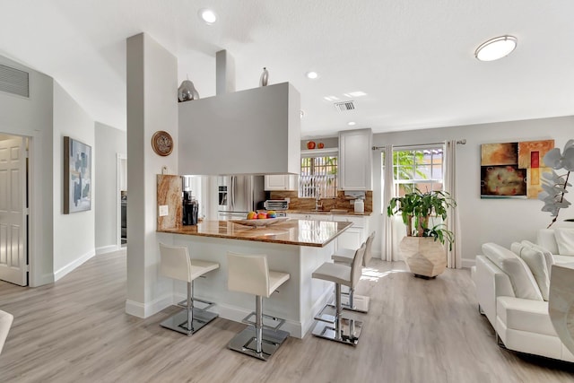 kitchen featuring stainless steel fridge, visible vents, a breakfast bar, light stone countertops, and backsplash