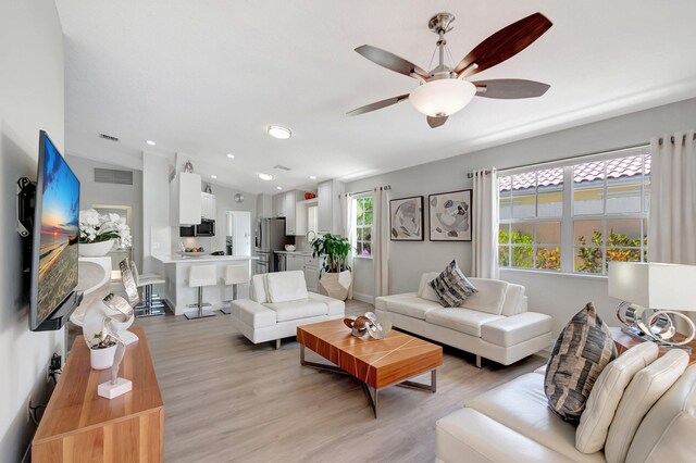 living room featuring light wood-style flooring, visible vents, vaulted ceiling, and baseboards