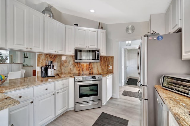 kitchen featuring stainless steel appliances, decorative backsplash, light wood-style flooring, and white cabinets