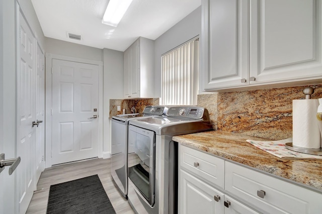 washroom with visible vents, cabinet space, washer and clothes dryer, and light wood finished floors