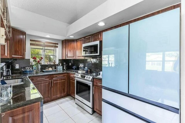 kitchen with stainless steel appliances, recessed lighting, decorative backsplash, light tile patterned flooring, and dark stone countertops