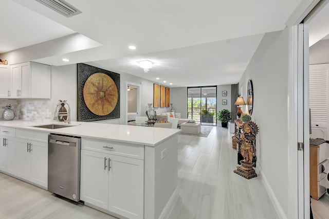 kitchen with white cabinets, open floor plan, light countertops, stainless steel dishwasher, and tasteful backsplash