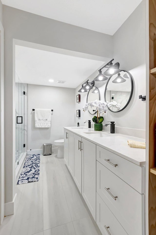 full bathroom featuring double vanity, toilet, a stall shower, a sink, and baseboards