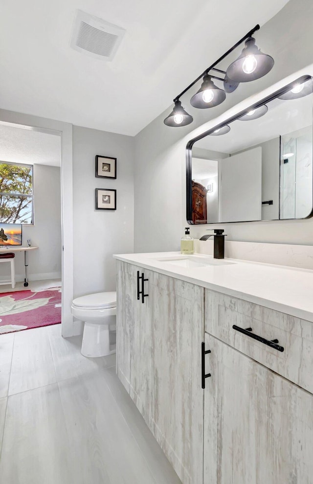 bathroom with vanity, toilet, baseboards, and visible vents