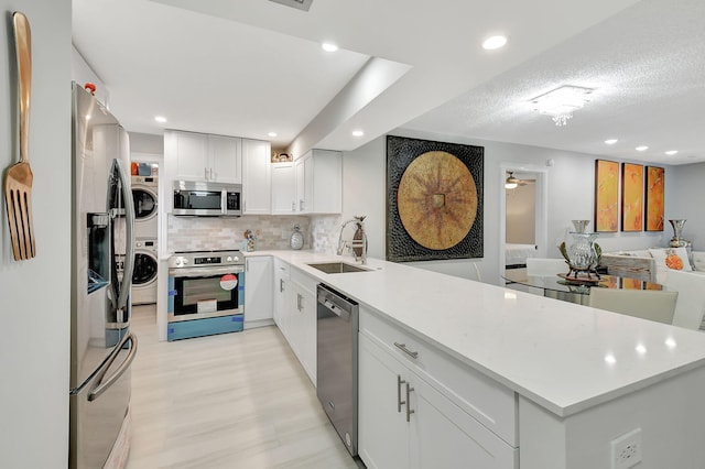 kitchen featuring stacked washer and dryer, a sink, white cabinetry, light countertops, and appliances with stainless steel finishes