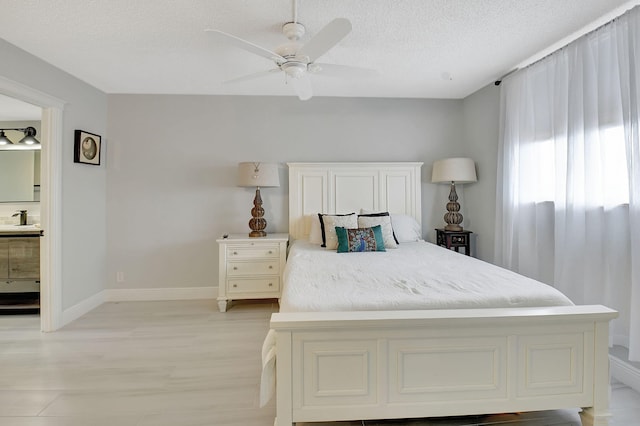 bedroom featuring light wood-style flooring, a ceiling fan, a sink, a textured ceiling, and baseboards