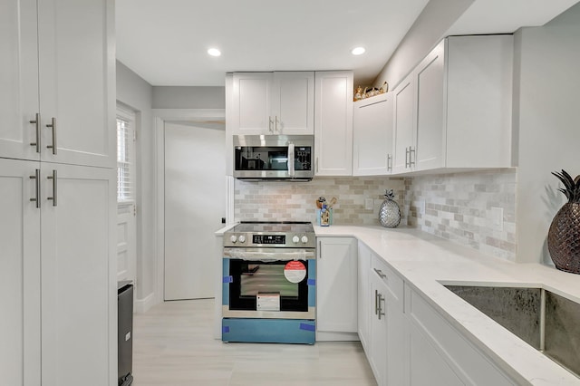 kitchen with appliances with stainless steel finishes, light stone countertops, white cabinetry, backsplash, and recessed lighting