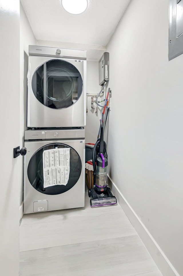 washroom with laundry area, stacked washer and clothes dryer, baseboards, and wood finished floors