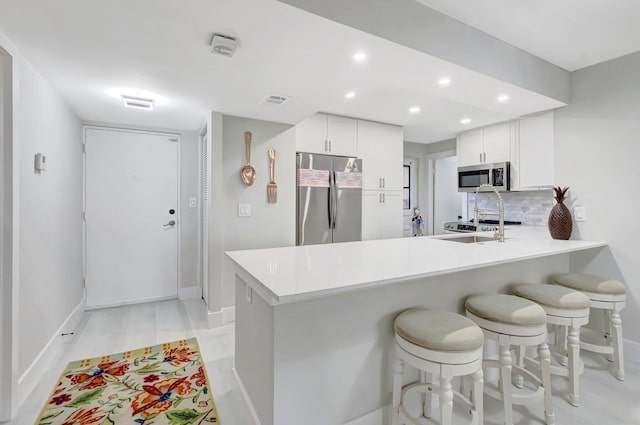 kitchen featuring a peninsula, a kitchen bar, stainless steel appliances, light countertops, and decorative backsplash