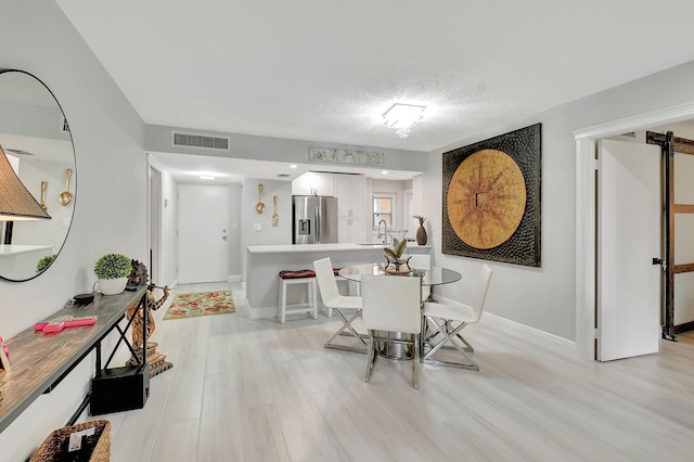 dining room with light wood-style floors, visible vents, a textured ceiling, and baseboards