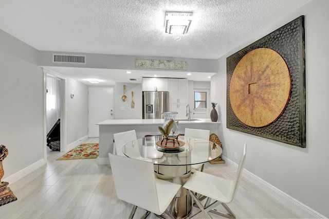 dining space featuring a textured ceiling, light wood-type flooring, visible vents, and baseboards