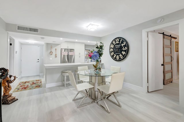 dining area with light wood-type flooring, visible vents, a barn door, and baseboards