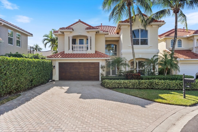 mediterranean / spanish house featuring a balcony, a garage, a tile roof, decorative driveway, and stucco siding