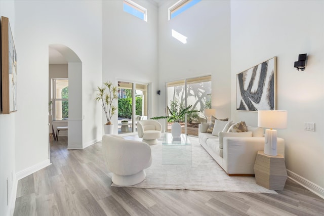 living room with arched walkways, light wood-type flooring, a towering ceiling, and baseboards