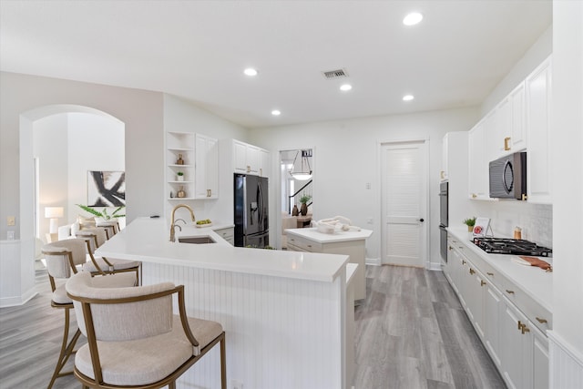 kitchen featuring a peninsula, appliances with stainless steel finishes, open shelves, and light countertops