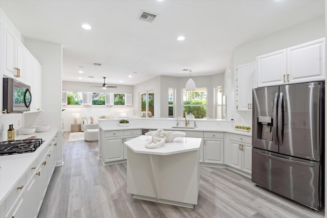 kitchen featuring open floor plan, hanging light fixtures, stainless steel appliances, light countertops, and white cabinetry