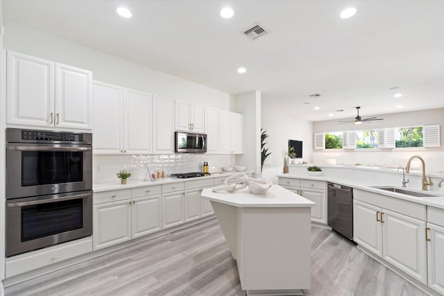 kitchen featuring light countertops, appliances with stainless steel finishes, white cabinetry, a kitchen island, and a sink