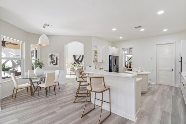 kitchen featuring stainless steel refrigerator with ice dispenser, open shelves, light countertops, hanging light fixtures, and white cabinetry