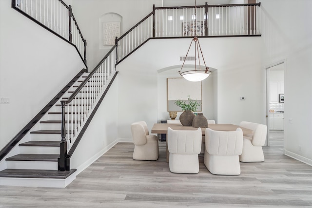 dining area with a high ceiling, stairway, light wood-type flooring, and baseboards