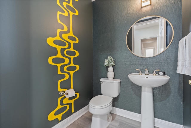 half bath with baseboards, a sink, toilet, and wood finished floors