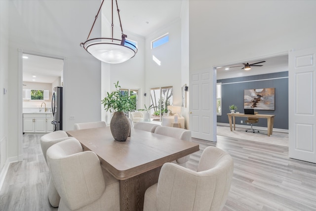 dining room featuring light wood finished floors, a towering ceiling, visible vents, and baseboards