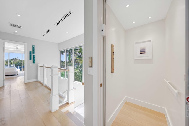 hall featuring light wood-style flooring, an upstairs landing, and visible vents