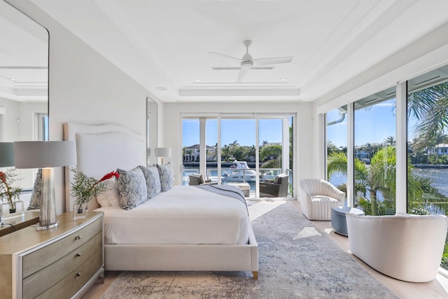 bedroom featuring access to exterior, ceiling fan, a tray ceiling, and wood finished floors