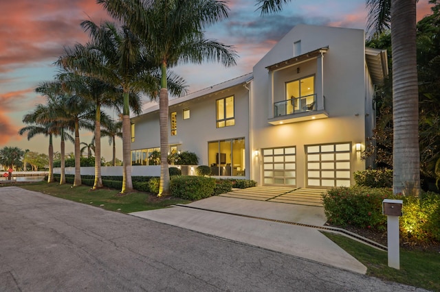 contemporary house with a balcony, a garage, driveway, and stucco siding