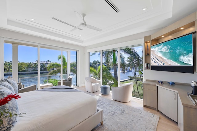 bedroom featuring a raised ceiling, a water view, and light wood-type flooring