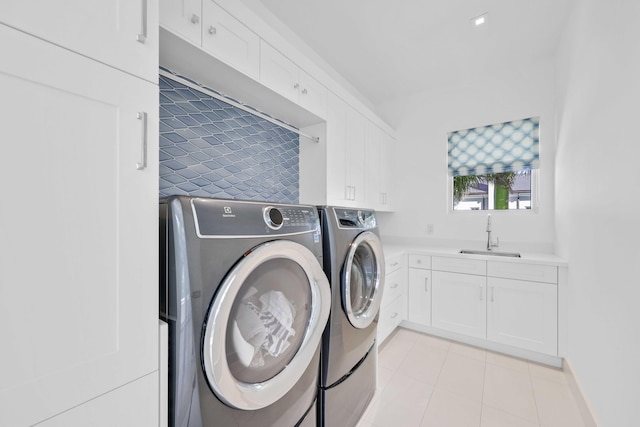 clothes washing area featuring a sink, cabinet space, light tile patterned flooring, and washer and clothes dryer