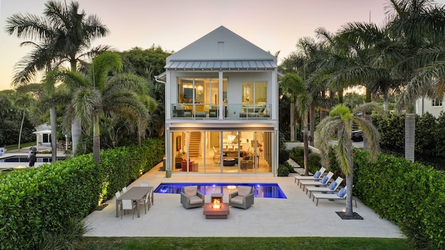 back of property at dusk with a balcony, an outdoor fire pit, a standing seam roof, a patio area, and metal roof