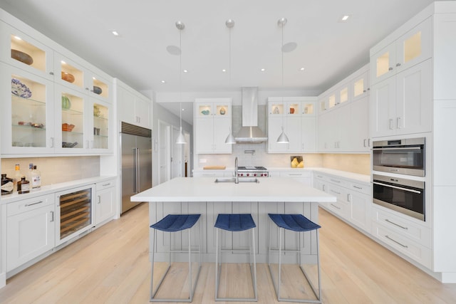 kitchen featuring a sink, decorative backsplash, wine cooler, appliances with stainless steel finishes, and wall chimney range hood