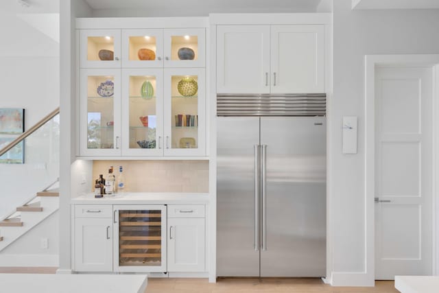 bar featuring stairs, wine cooler, built in fridge, a dry bar, and backsplash