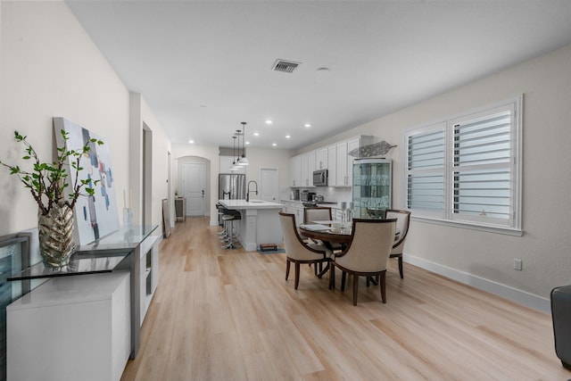 dining room with light wood finished floors, baseboards, visible vents, arched walkways, and recessed lighting