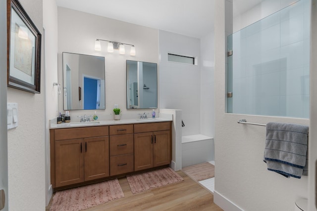 full bathroom featuring a walk in shower, double vanity, wood finished floors, and a sink