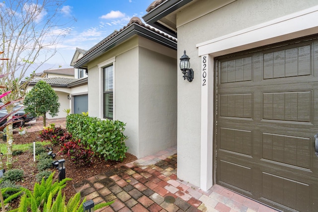 entrance to property featuring a garage, a tile roof, and stucco siding