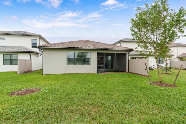 back of property with a sunroom, a tile roof, a lawn, and fence