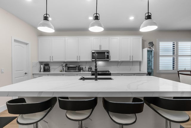 kitchen with a kitchen island with sink, white cabinets, stainless steel microwave, and hanging light fixtures