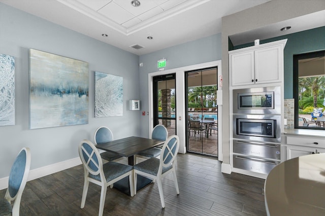 dining area with a tray ceiling, plenty of natural light, dark wood finished floors, and baseboards