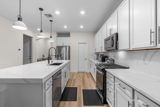 kitchen with stainless steel appliances, visible vents, white cabinetry, hanging light fixtures, and a center island with sink