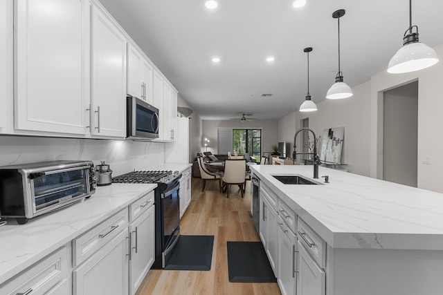 kitchen with black gas stove, a kitchen island with sink, stainless steel microwave, and white cabinets