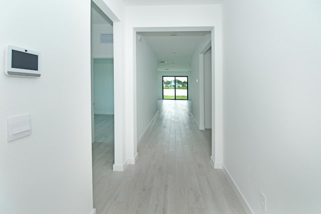 hall featuring light wood-style floors, visible vents, and baseboards