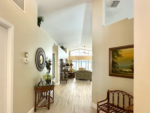 hallway with vaulted ceiling, wood finished floors, visible vents, and baseboards