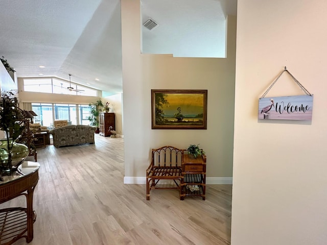 hall with lofted ceiling, visible vents, baseboards, and wood finished floors