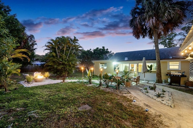 back of house at dusk with a lawn, a patio, a fire pit, and stucco siding