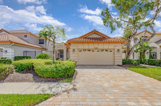 mediterranean / spanish-style house featuring an attached garage, fence, a tile roof, decorative driveway, and stucco siding