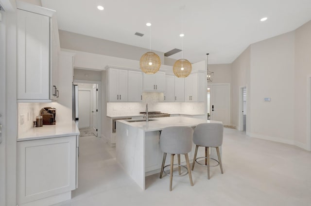 kitchen featuring a breakfast bar, a kitchen island with sink, light countertops, pendant lighting, and backsplash